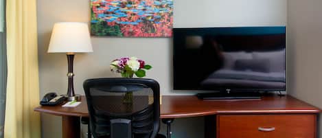 Habitación de hotel con escritorio, lámpara, teléfono, televisión y un cuadro en la pared.