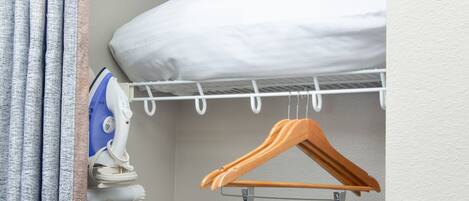A neatly organized closet with a hanging rack, an ironing board, and a white pillow.