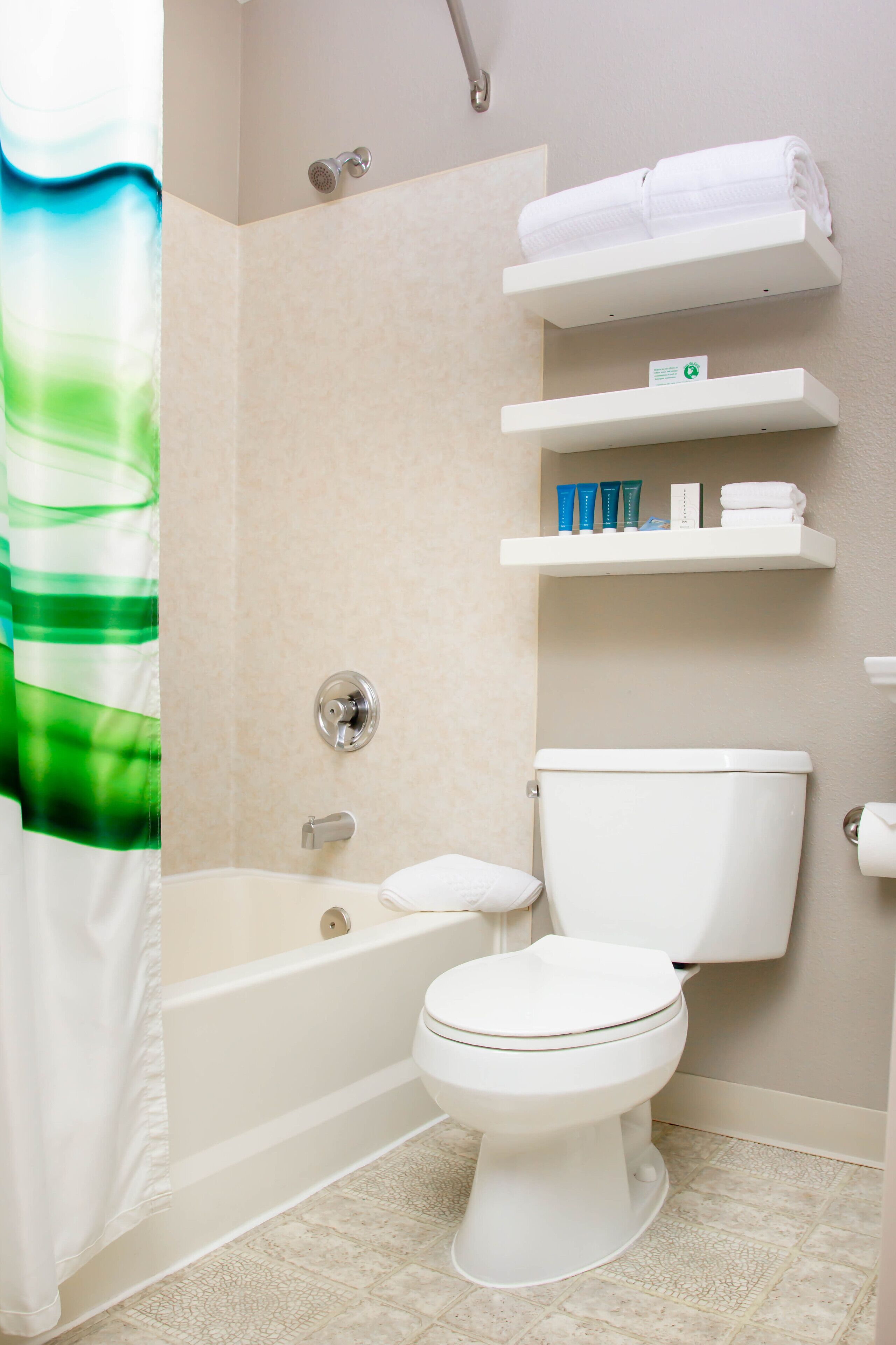 A bathroom with a bathtub, toilet, and shower curtain. There are shelves with toiletries and a towel rack.