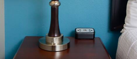 A bedside table with a lamp, a power strip, and a drawer.
