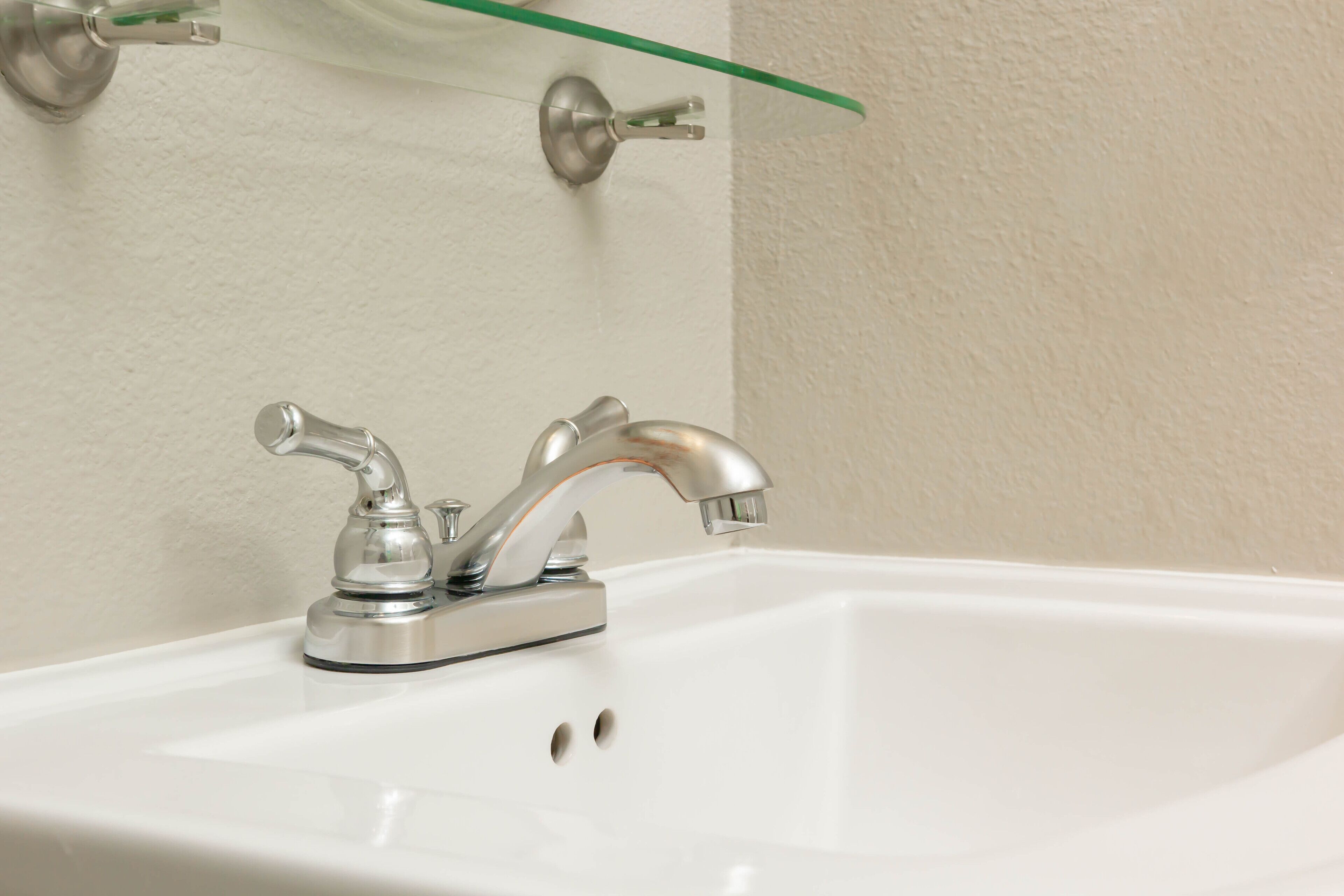 A bathroom sink with a chrome faucet and a glass shelf above it.