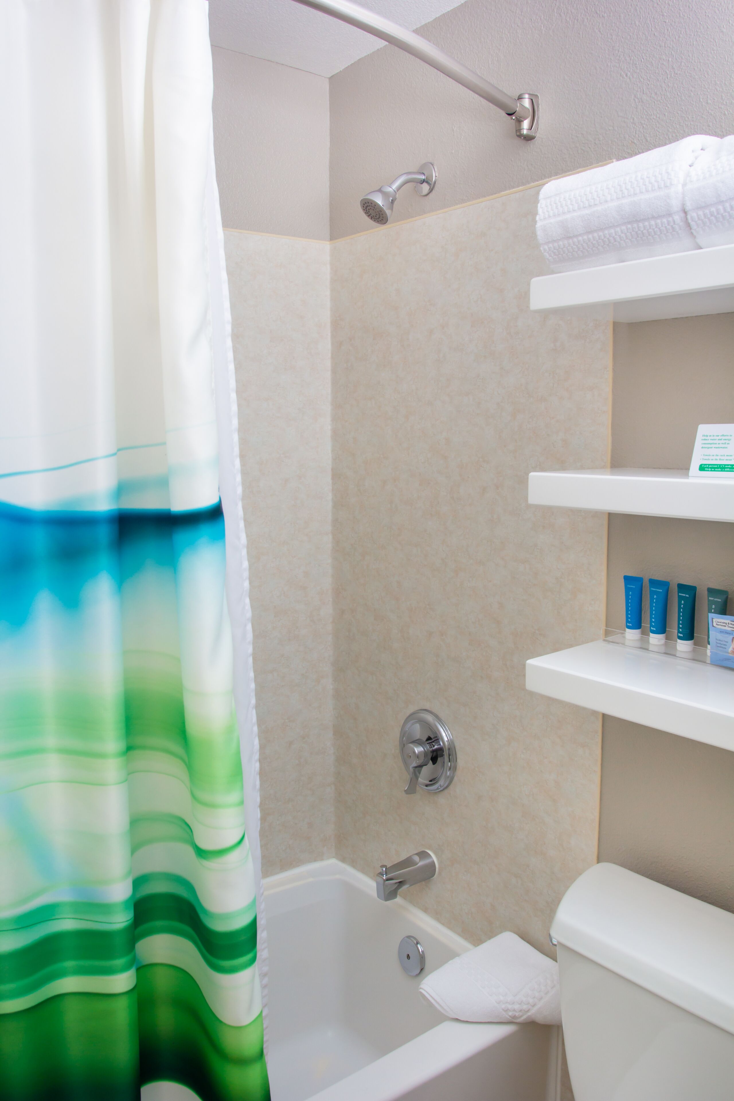 A bathroom with a shower, bathtub, and toilet. There are shelves with toiletries.