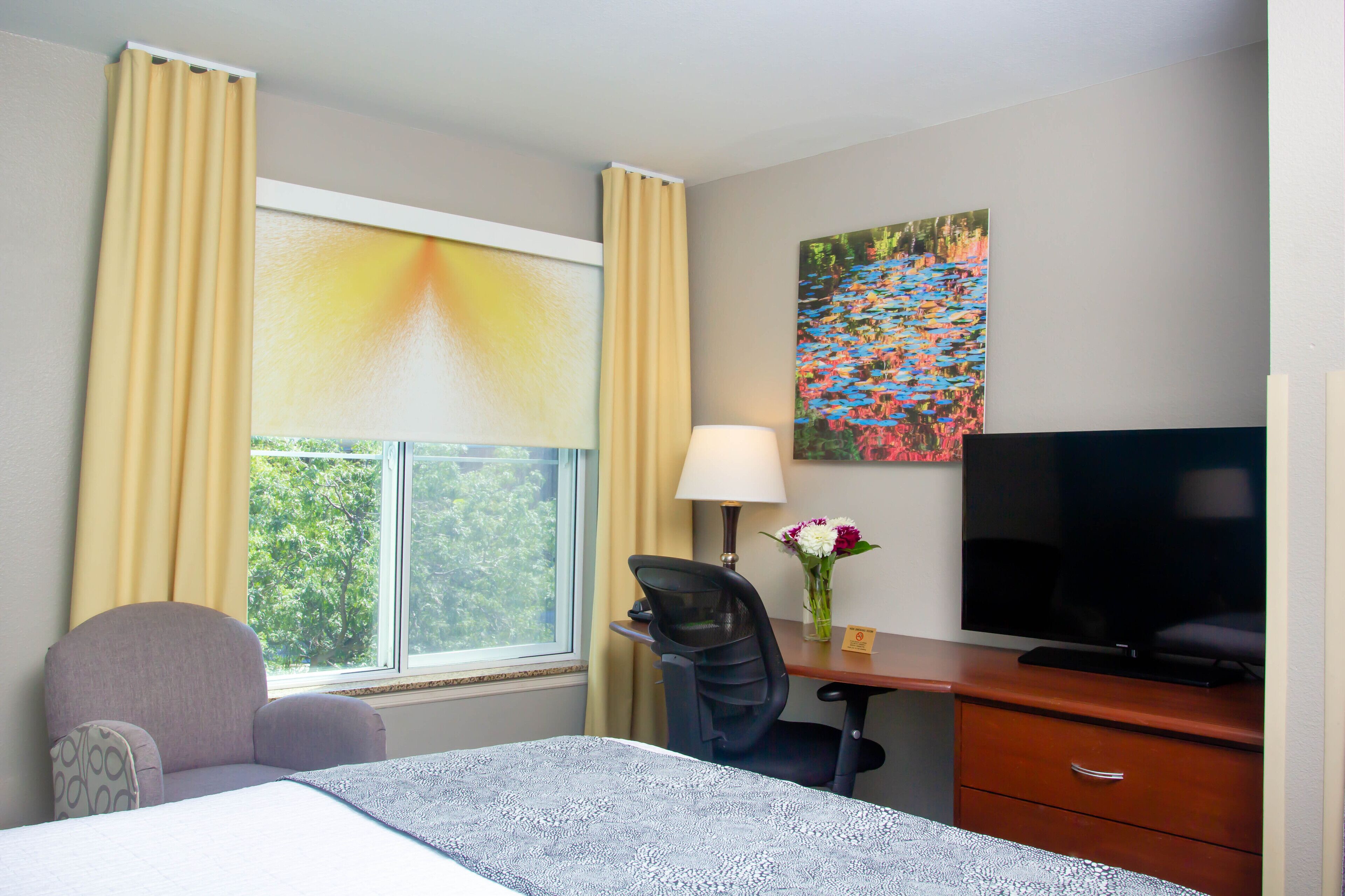 Une chambre d’hôtel avec un lit, un bureau avec une lampe, une télévision et une fenêtre avec des rideaux.