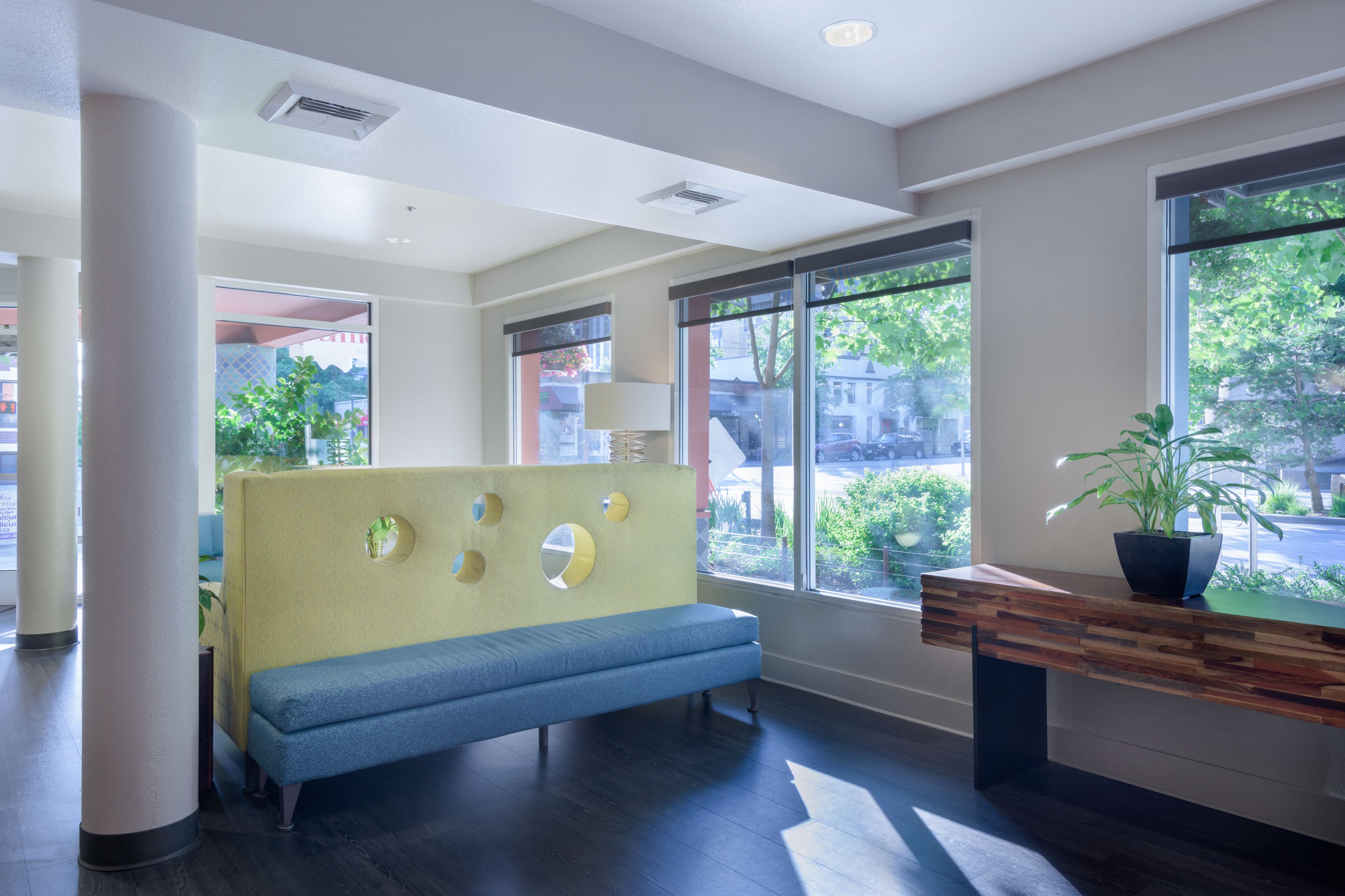 A modern reception area with a blue bench, a wooden reception desk, and large windows offering a view of the outdoors.