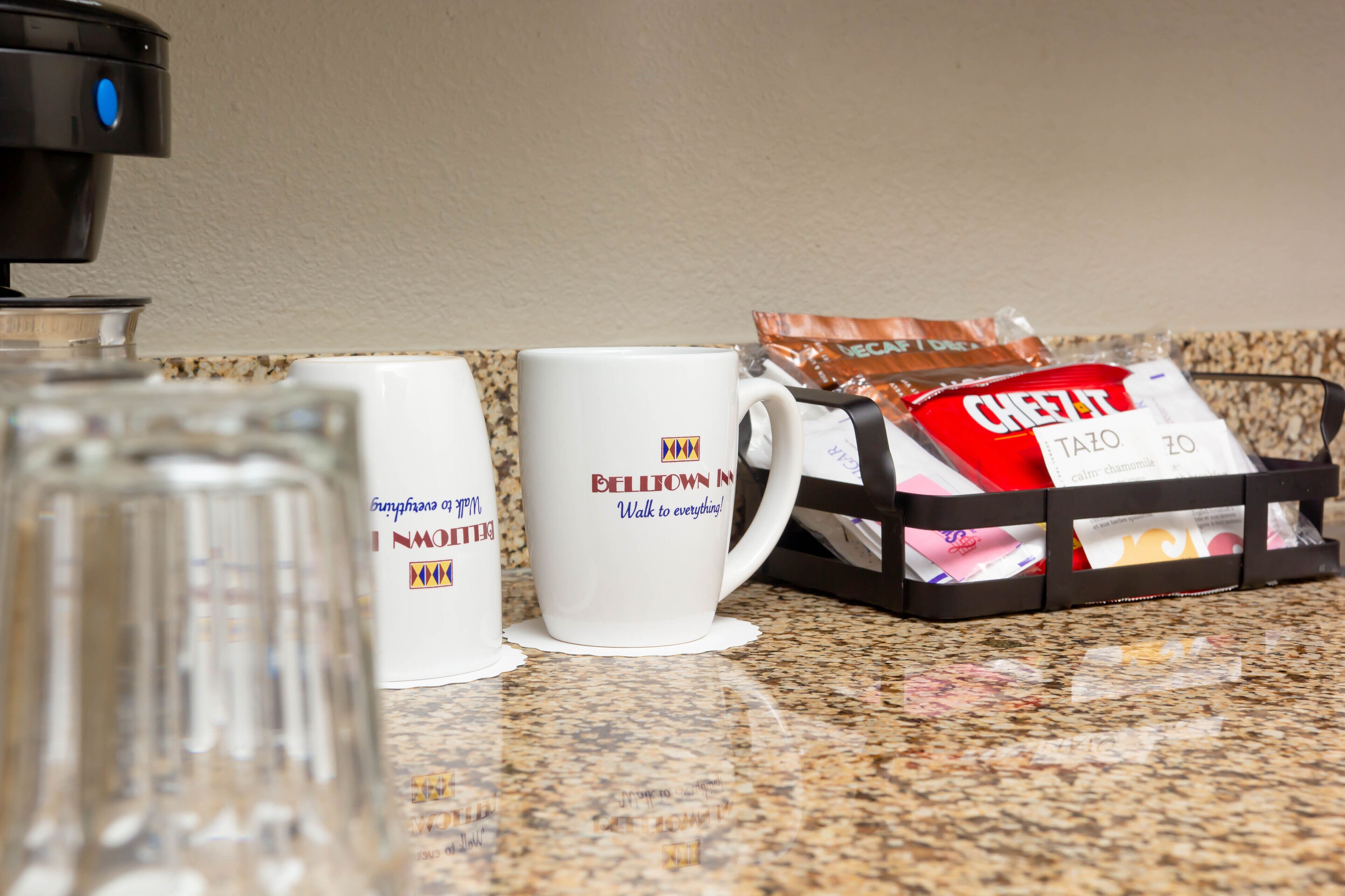 A kitchen counter with a coffee maker, two mugs, and a bag of Cheez-It crackers.