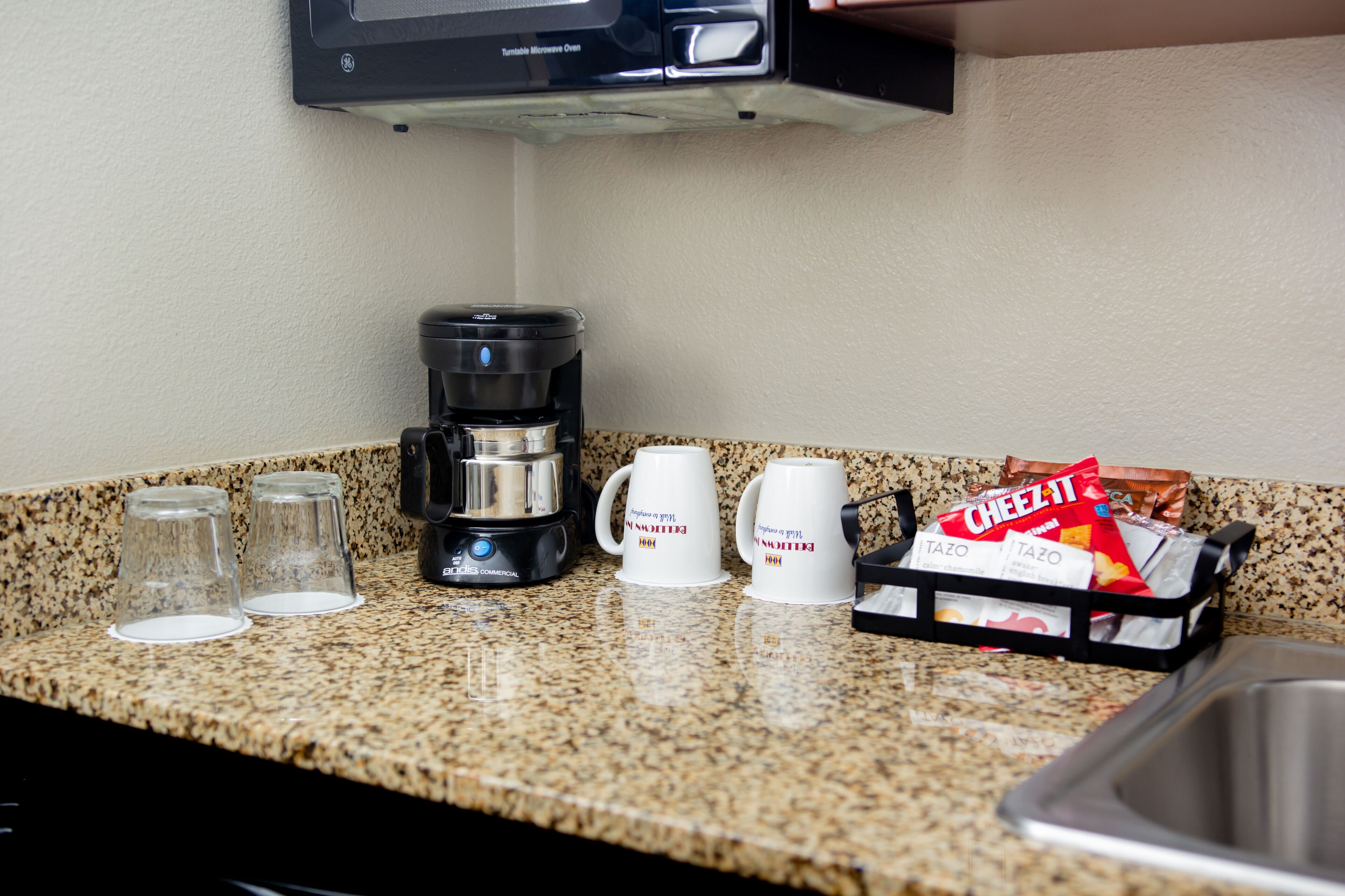 A kitchen counter with a coffee maker, two coffee mugs, and a bag of Cheez-It crackers.