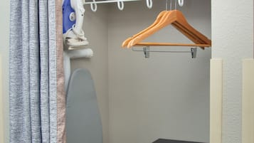 A compact room with a bunk bed, an ironing board, a hanging clothes rack, and a self-service laundry machine.