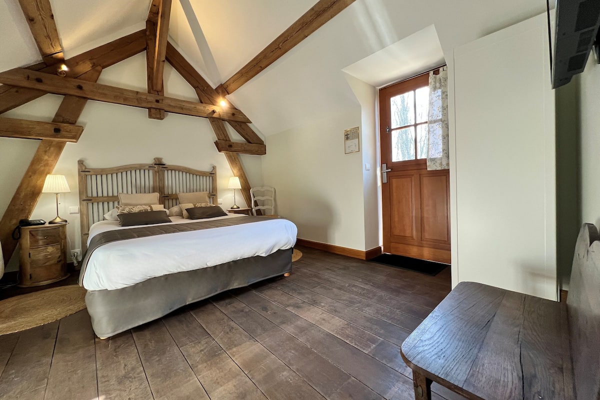 A bedroom with a wooden ceiling, a bed, a chair, and a door.