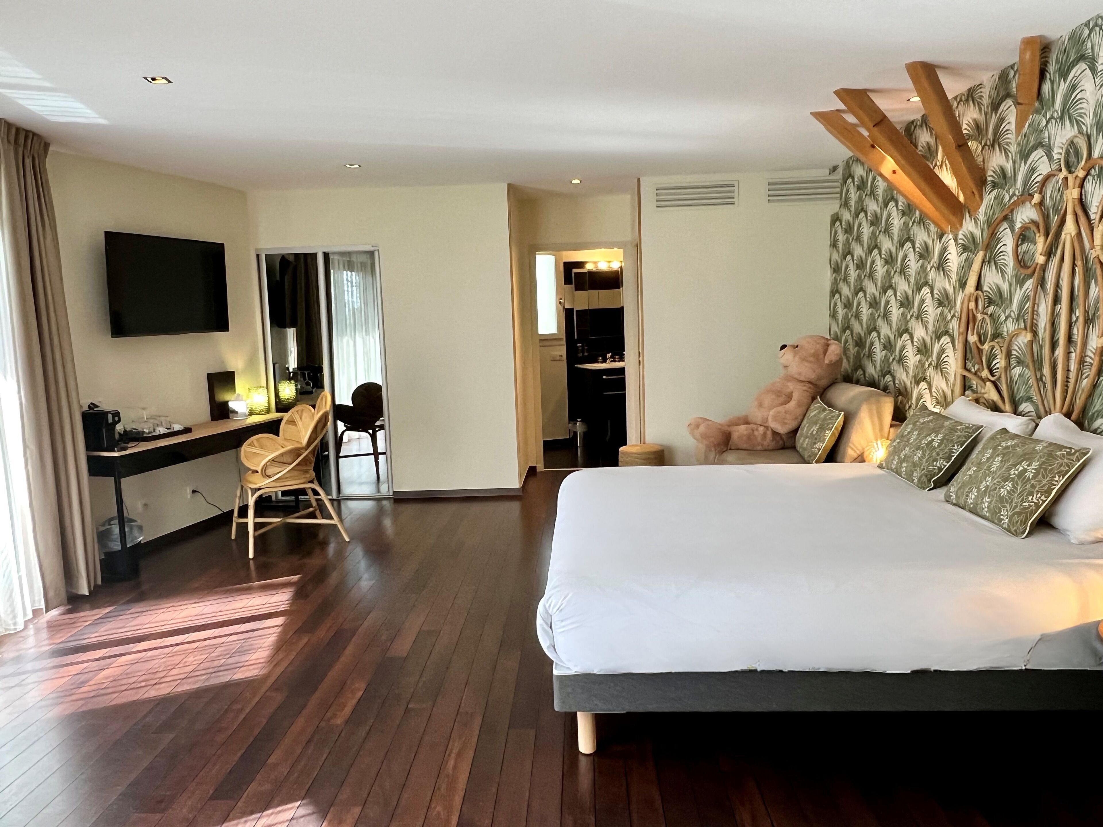 A hotel room with a large bed, a desk with a chair, a television, and a wardrobe.