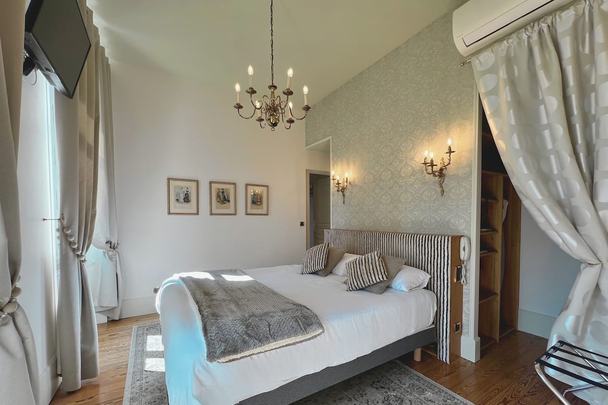 A bedroom with a large bed, a chandelier, wall-mounted lights, and a patterned rug.