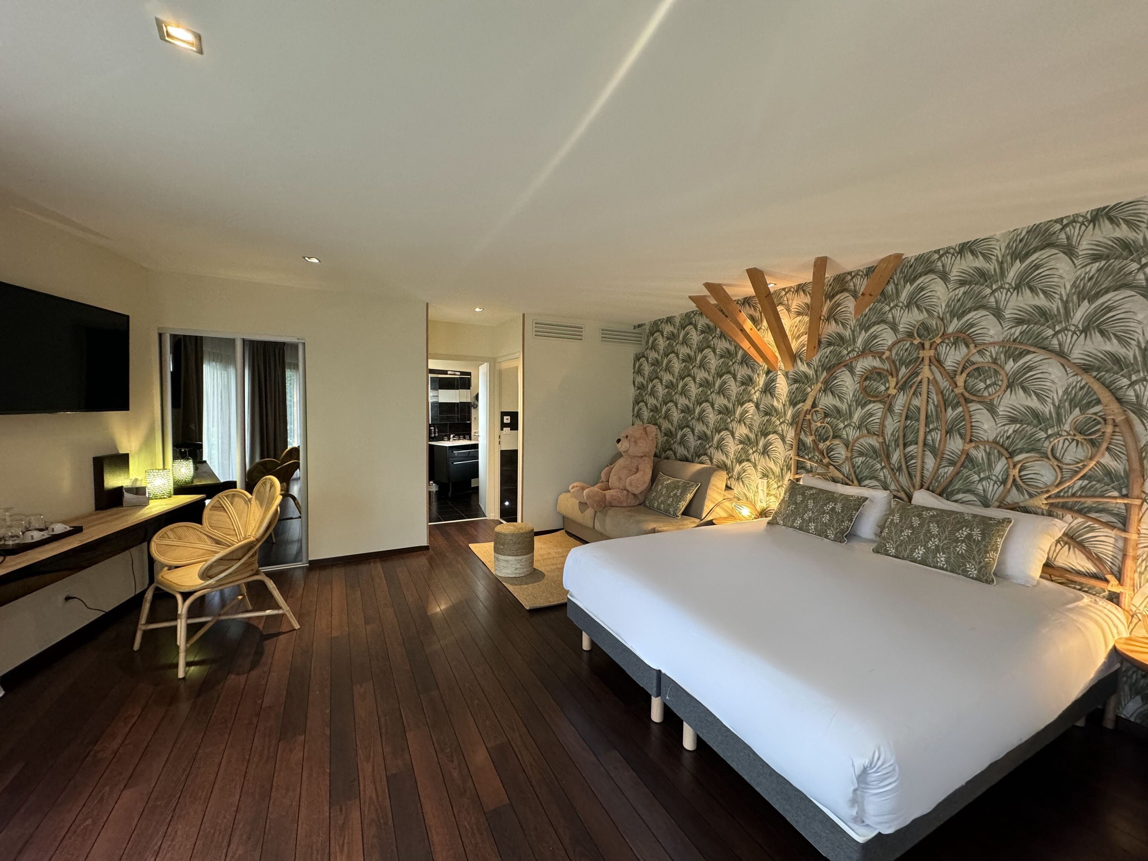 Habitación de hotel moderna con una cama grande, un escritorio con silla, televisión y un baño visible a través de una puerta abierta.