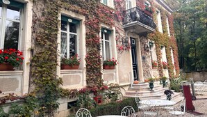 Un edificio histórico con paredes cubiertas de hiedra, ventanas grandes y mesas al aire libre.