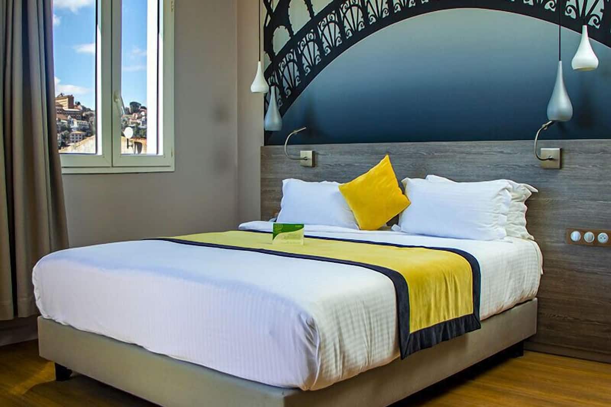 A hotel room with a large bed, a view of the city through the window, and a unique headboard design.