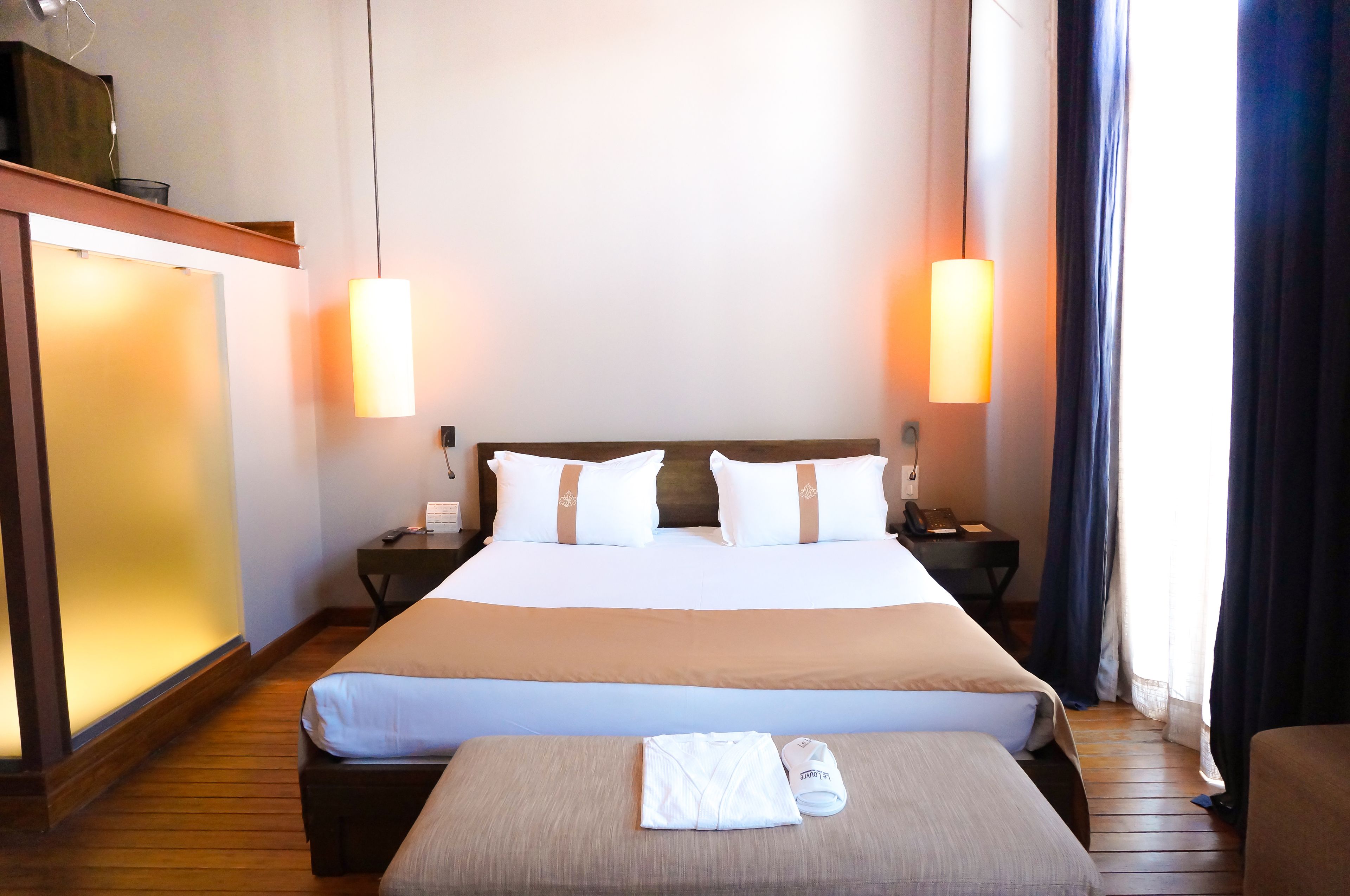 A hotel room with a large bed, bedside tables, a desk, and a window with curtains.