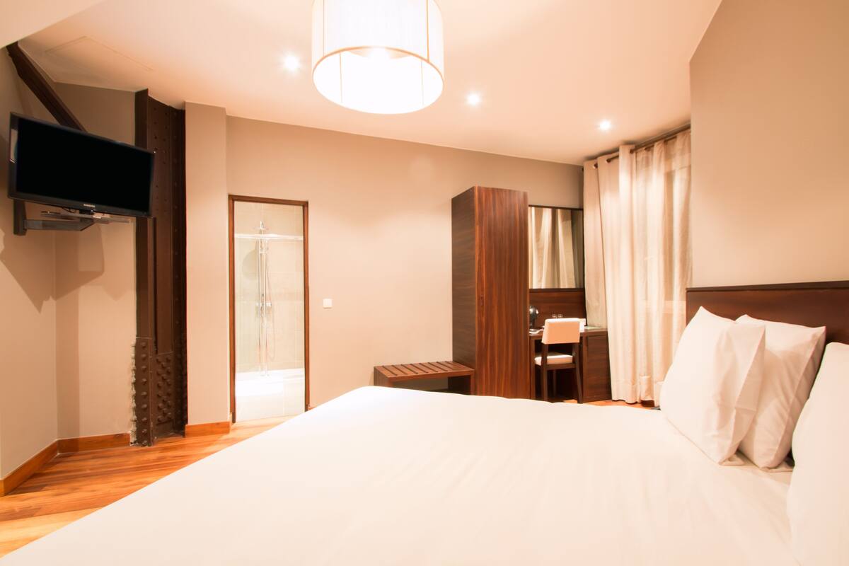 A hotel room with a large bed, a desk with a chair, a television mounted on the wall, and a wardrobe.
