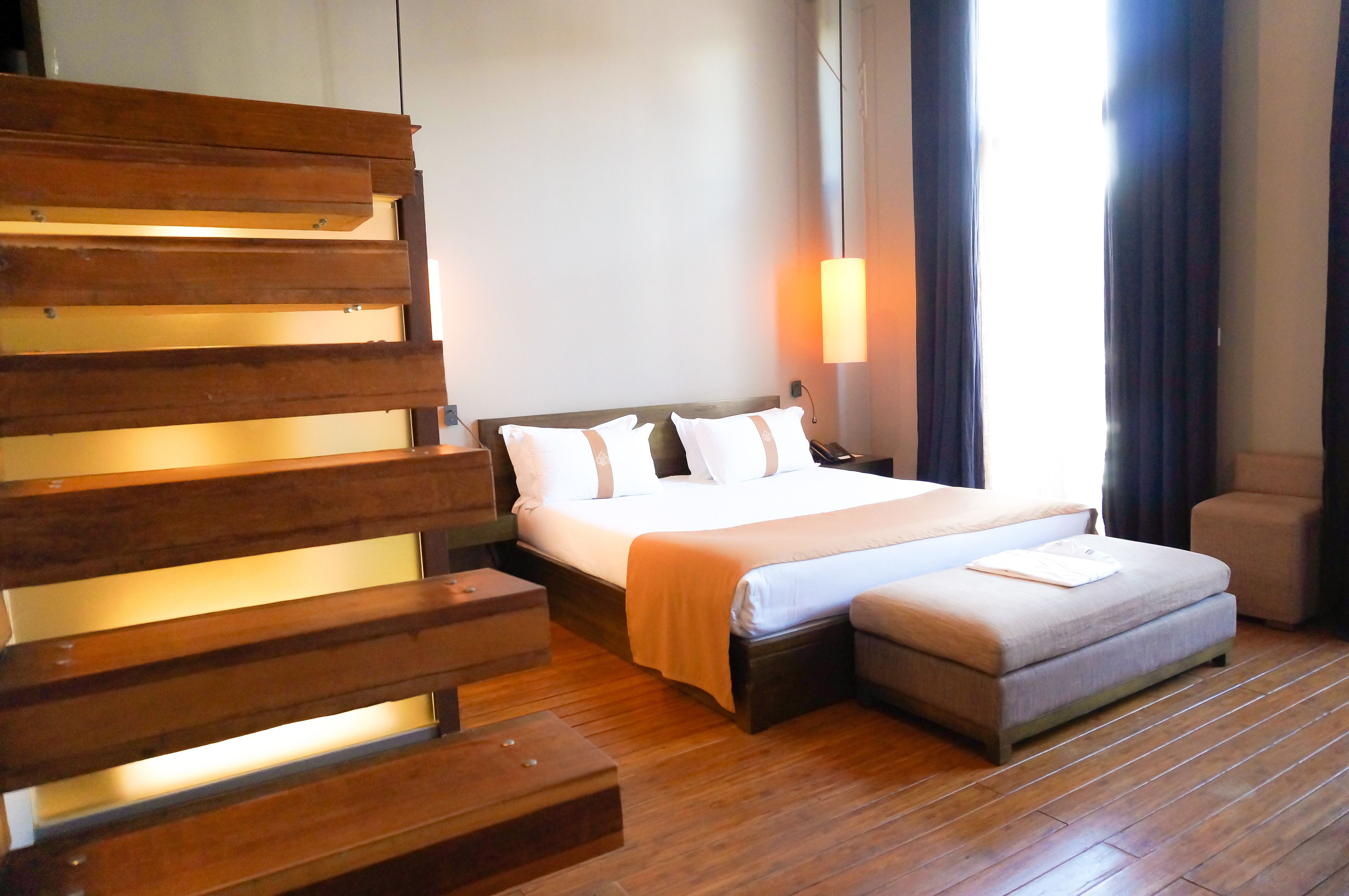 Een hotelkamer met een houten bankje, een bed met wit beddengoed, een nachtkastje en een nachttafel.
