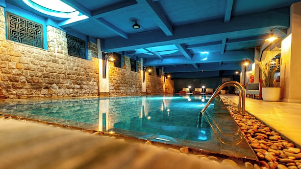 An indoor swimming pool with stone walls and a stone pool edge, surrounded by a pebble-lined walkway.