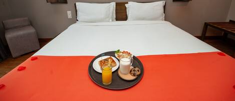A hotel room with a neatly made bed, a tray with breakfast items, and two wall-mounted lamps.