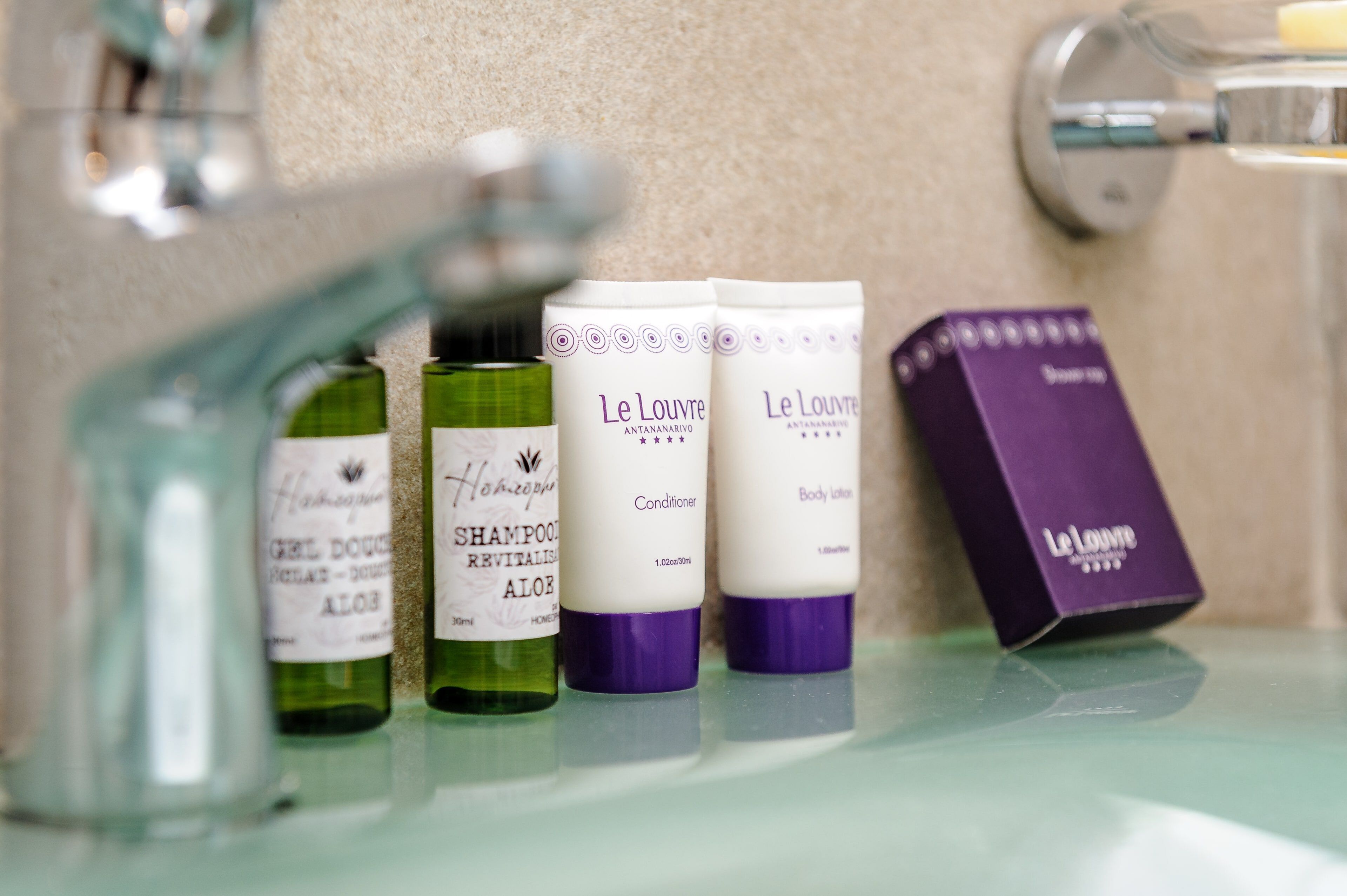 Un estante de baño con varios productos Le Louver, incluyendo champú, acondicionador y loción corporal.