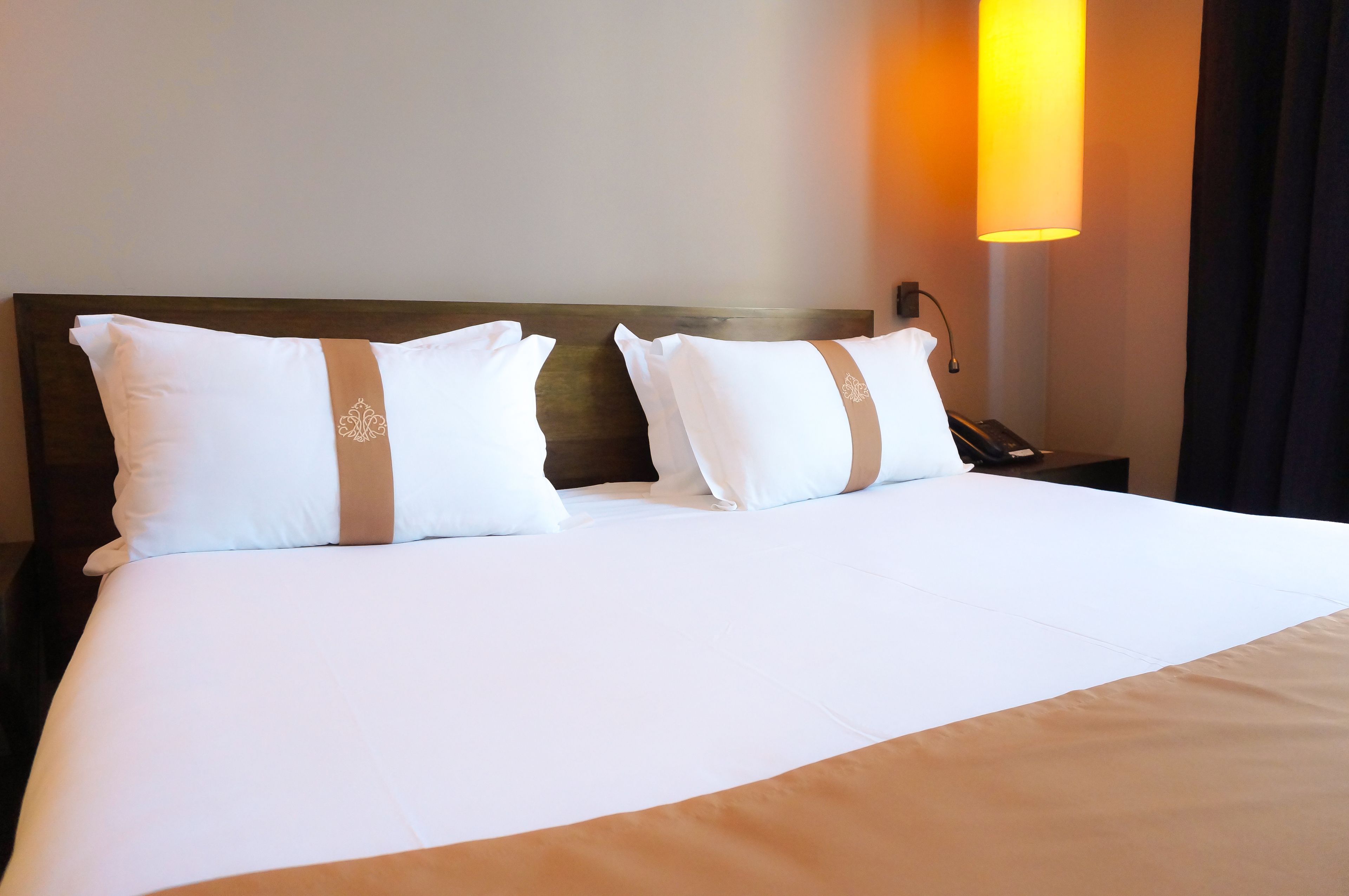A neatly made bed with white bedding and two pillows, a bedside table with a lamp, and a wall-mounted light fixture.