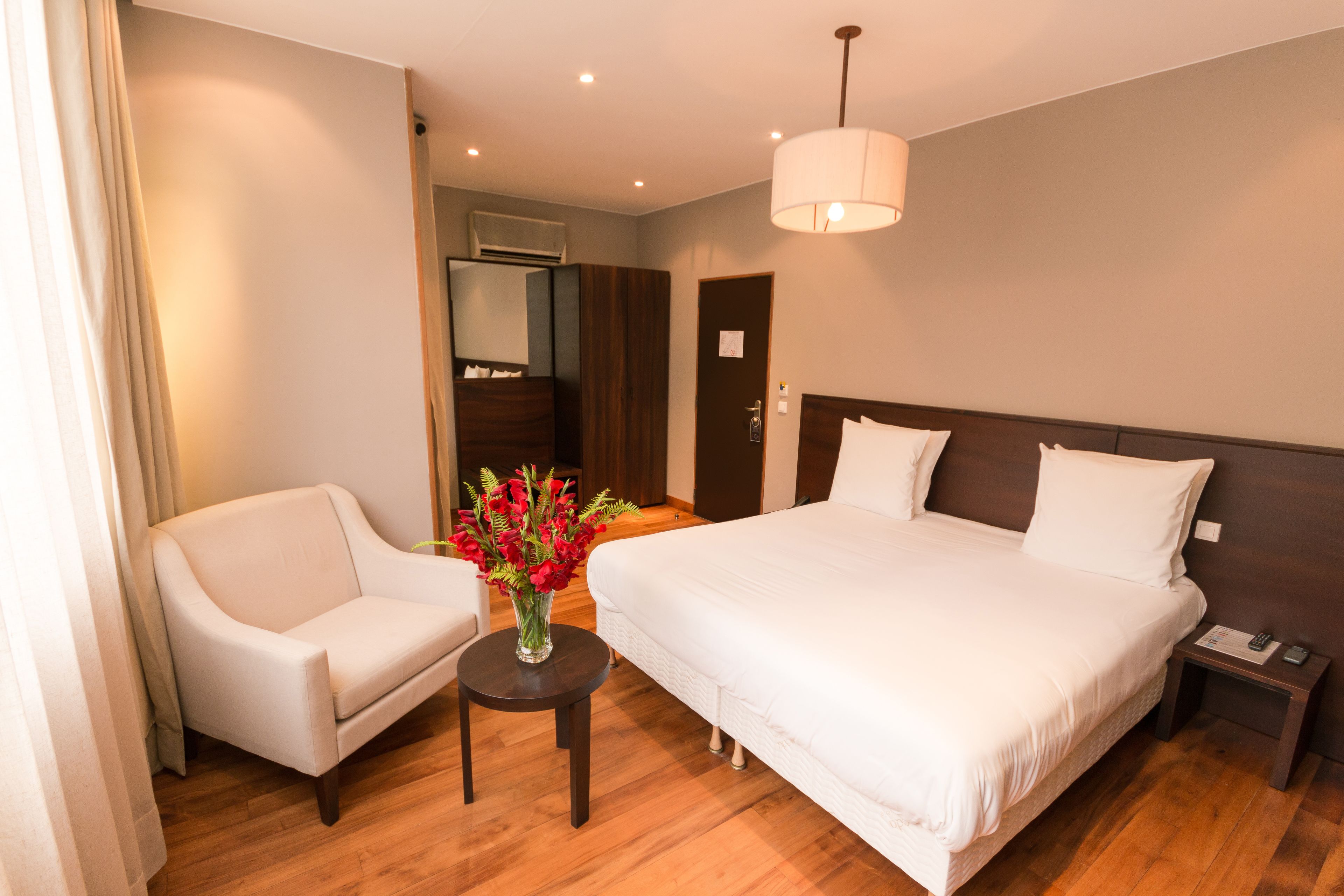 Habitación de hotel con una cama grande, una silla, una mesita con un florero y una mesita de noche con un teléfono.