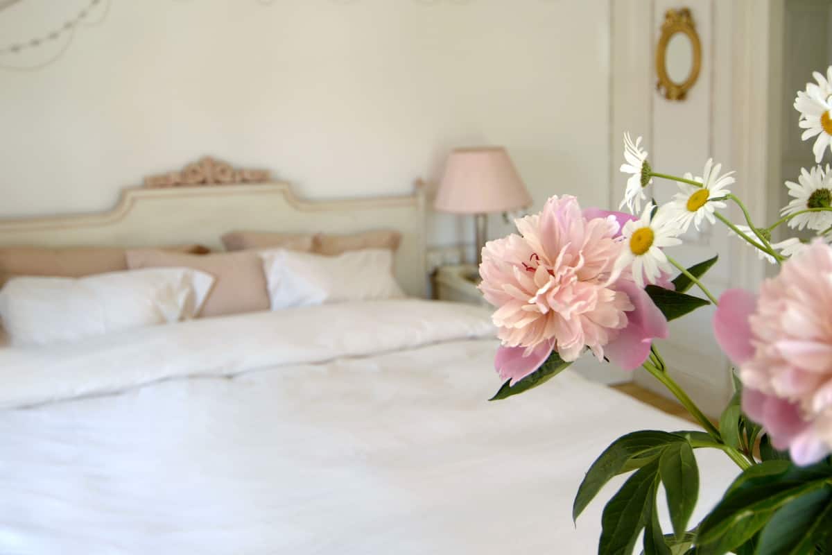 Un dormitorio con cama, almohadas, una mesita de noche, una lámpara y un espejo en la pared.