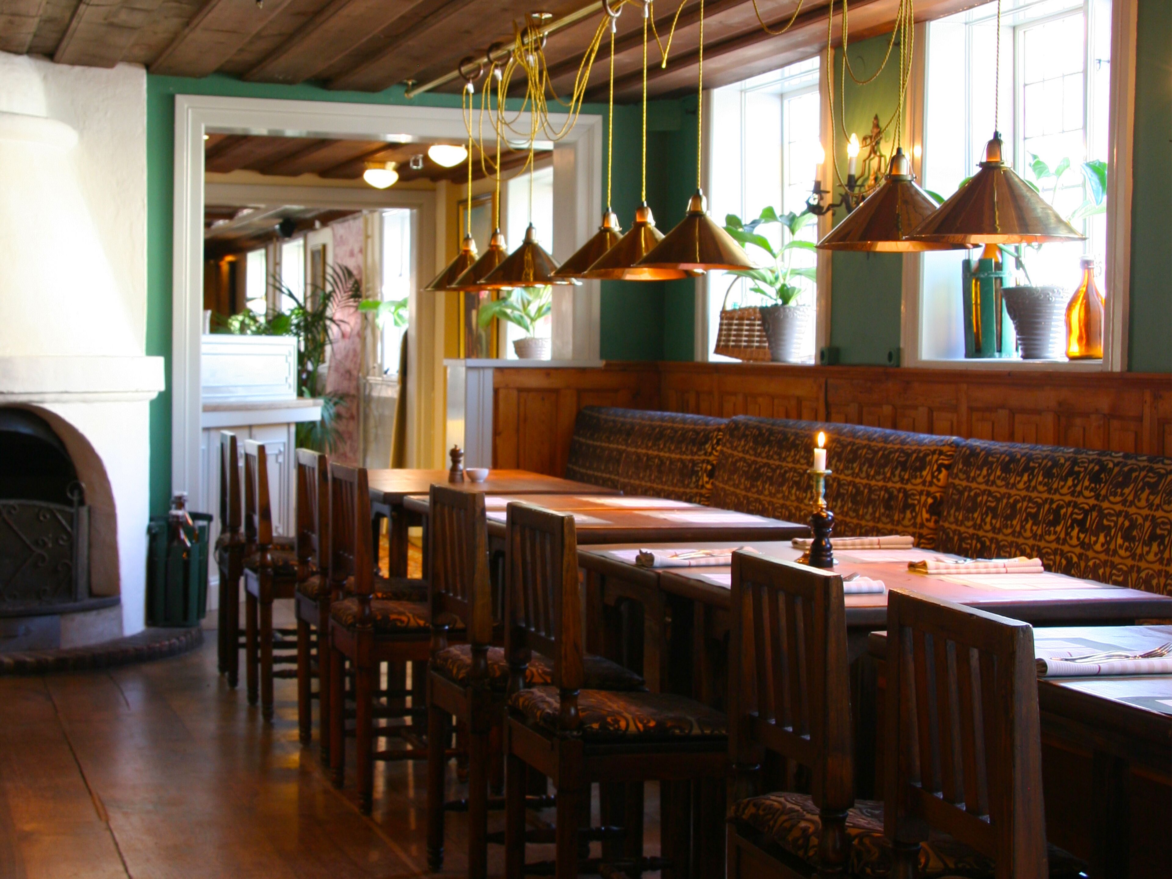 Un restaurante con mesas y sillas de madera, luces colgantes y un banco con estampado.