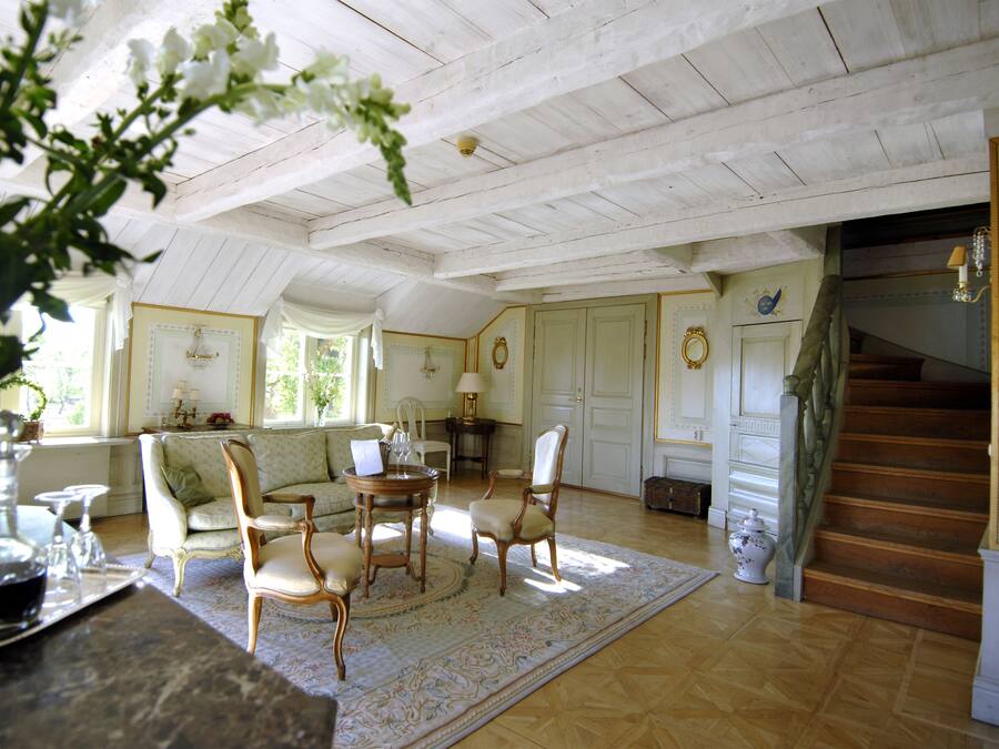 A spacious living room with a high ceiling, a dining area with a round table, and a staircase leading to another level.