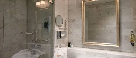 A bathroom with a glass-enclosed shower, a sink, and a large mirror with a gold frame.