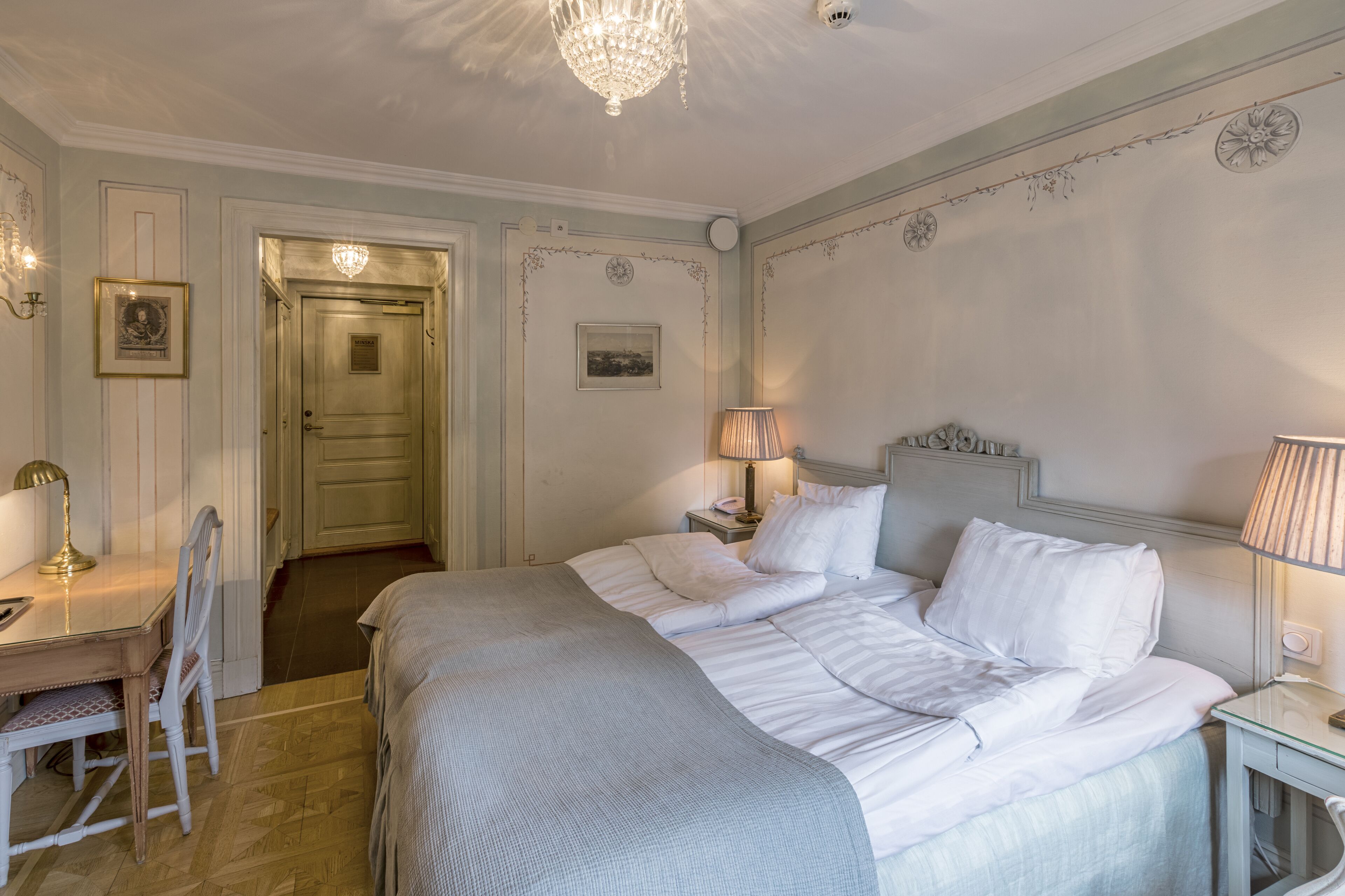 A neatly arranged bedroom with a bed, bedside lamps, a desk, and a chair.