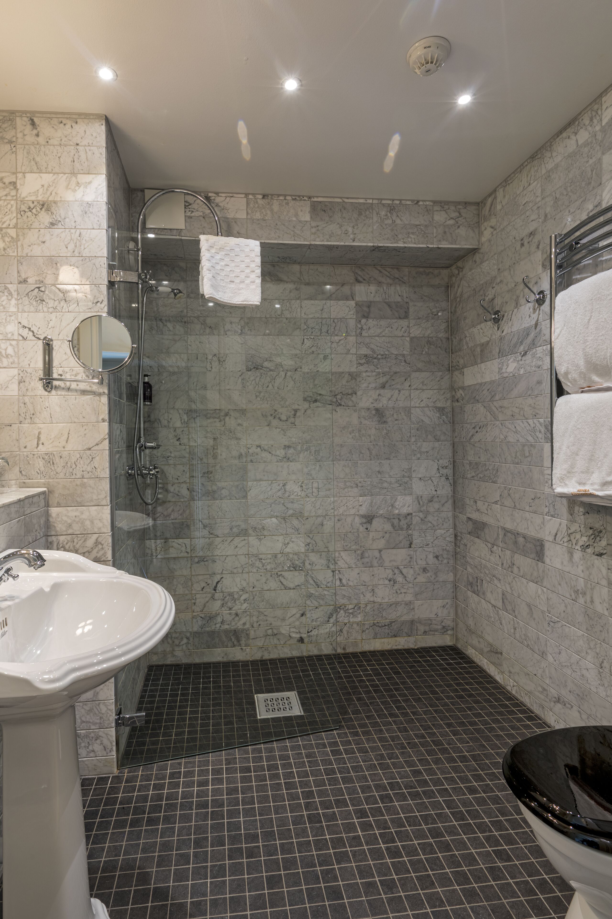 A modern bathroom with a glass-enclosed shower, a pedestal sink, and a toilet.