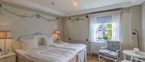 A bedroom with two beds, a nightstand, a chair, a table, and a chandelier.