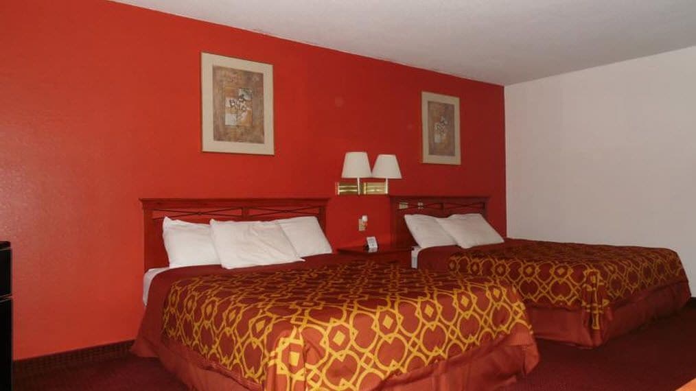 A hotel room with two beds, red walls, and two framed pictures.