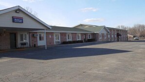 A motel with a signboard, a covered parking area, and a building with a brick facade. - American Inn & Suites (Boone)