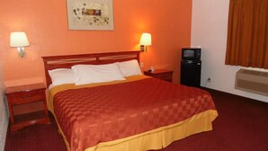 A hotel room with a large bed, two bedside tables, a TV, and a heater. - American Inn & Suites (Boone)