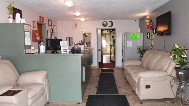 A hotel lobby with a reception desk, a sofa, a dining area, and a TV mounted on the wall. - American Inn & Suites (Boone)