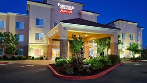 Un hotel Fairfield Inn & Suites Marriott con entrada cubierta, jardín ajardinado y cielo despejado.