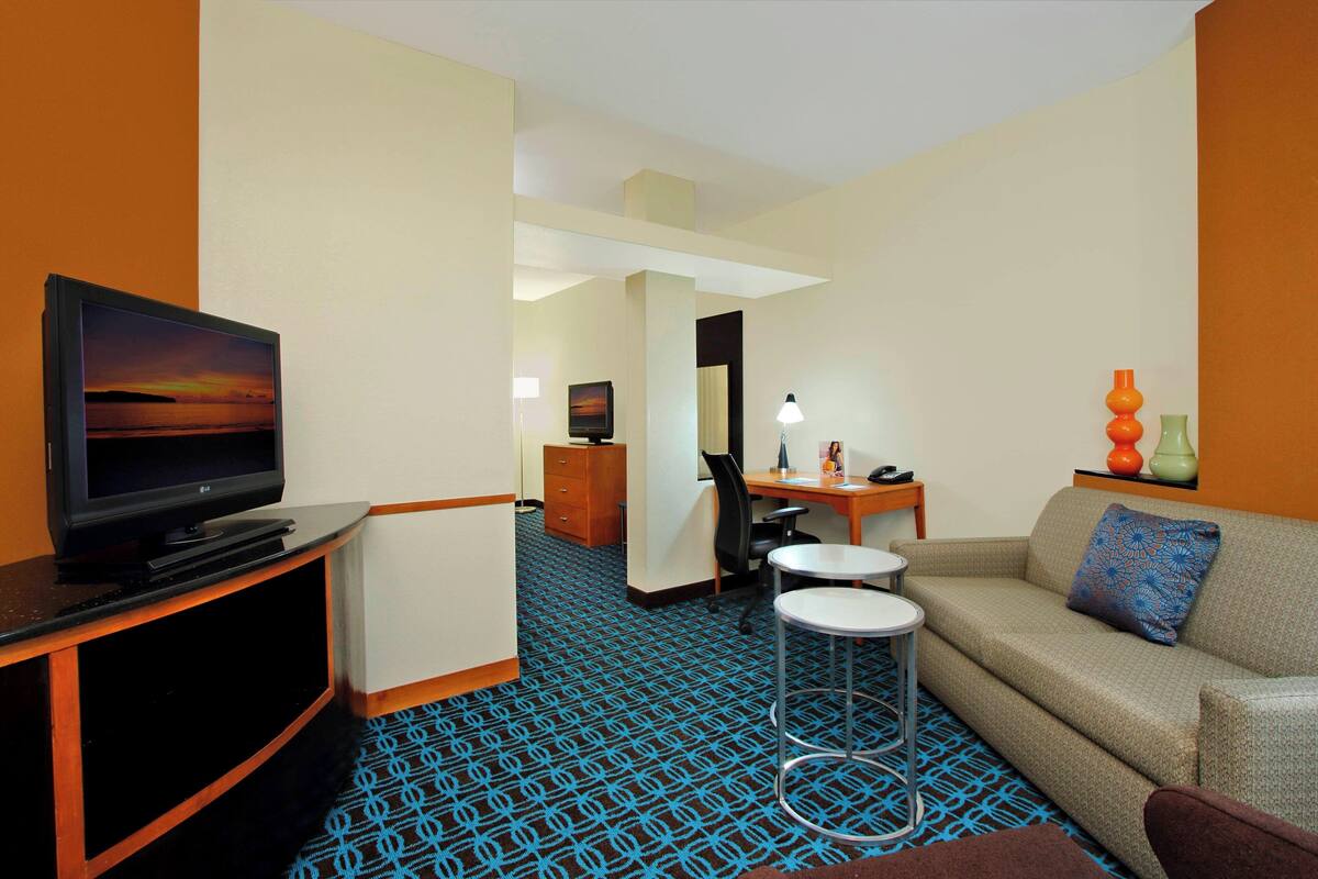 A hotel room with a television, a sofa, a desk, and a chair.
