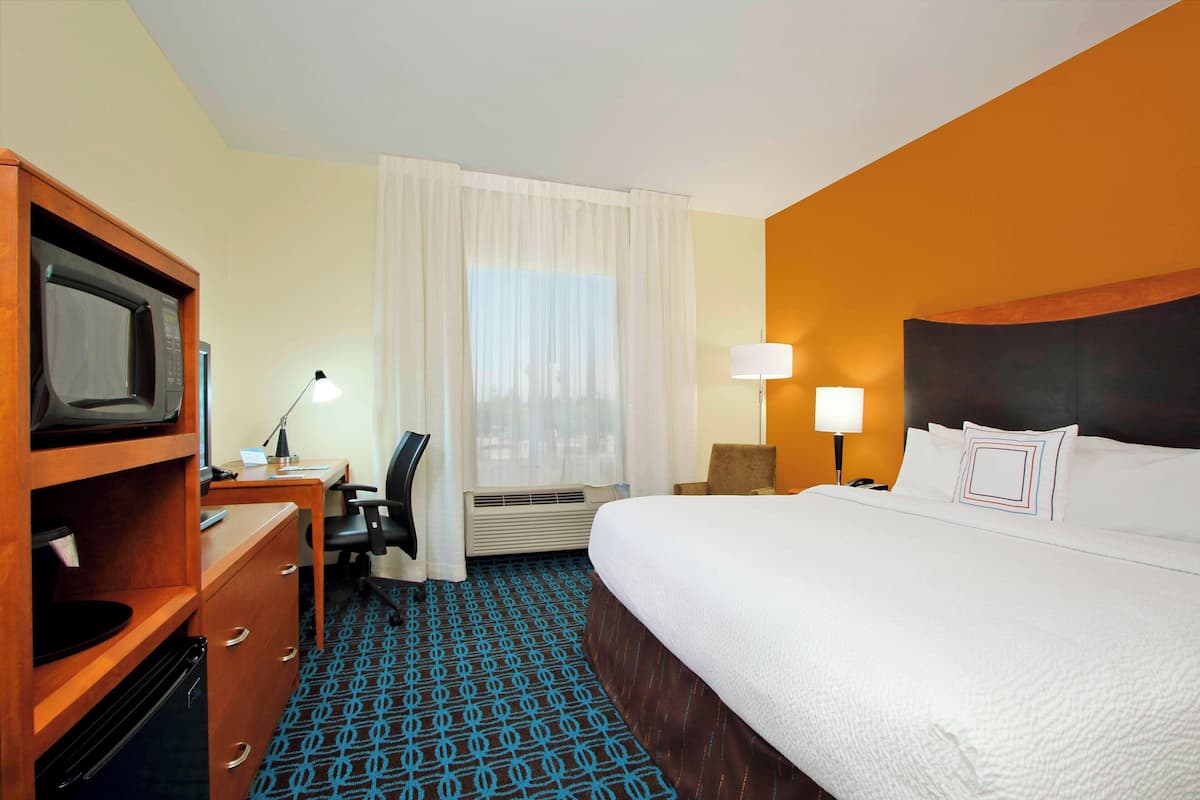 A hotel room with a bed, a desk with a chair, a television, and a lamp.