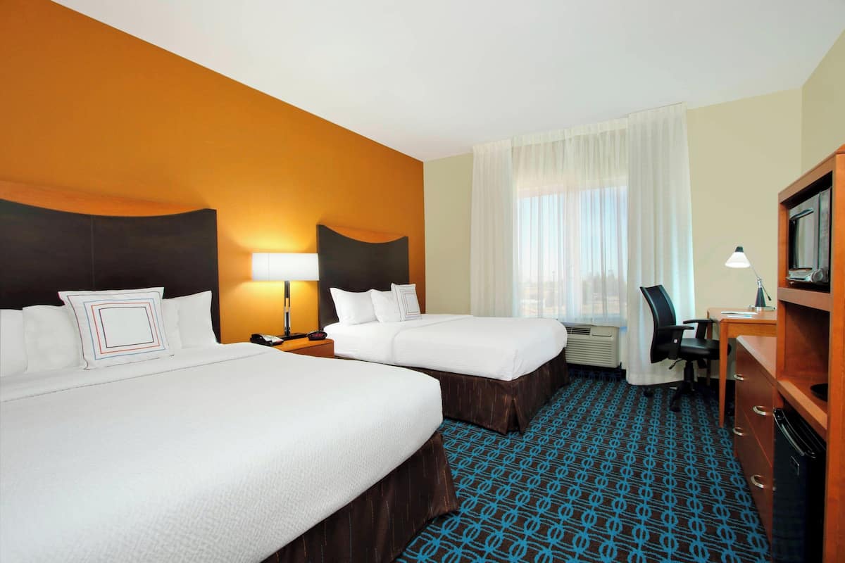 A hotel room with two beds, a desk, a chair, a TV, and a window with curtains.