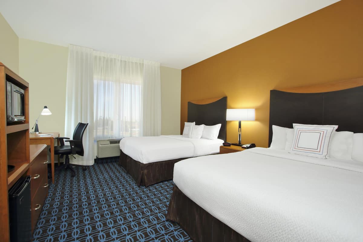 A hotel room with two beds, a desk, a chair, a TV, and a window with curtains.