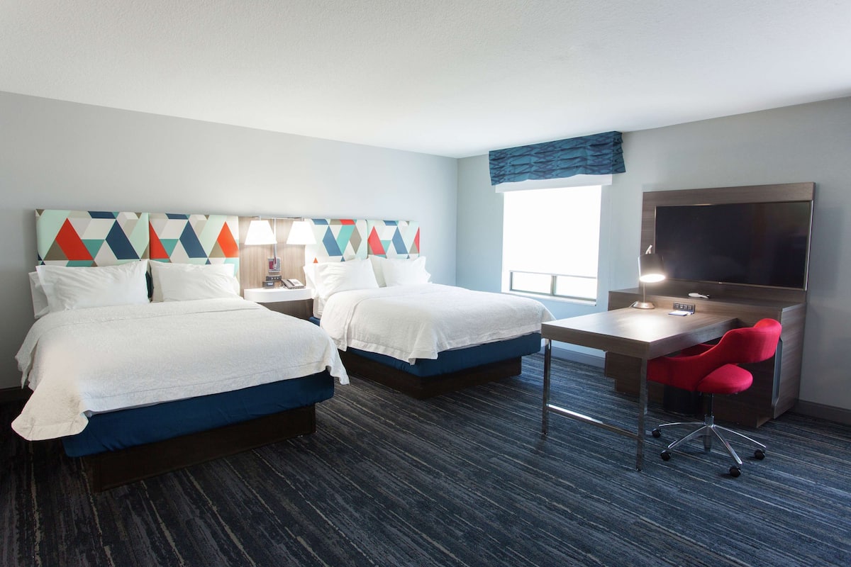 A hotel room with two beds, a desk, a TV, and a red chair.