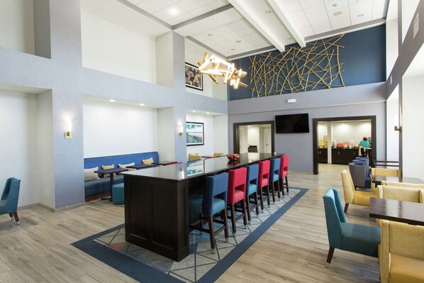 A modern hotel lobby with a central bar, seating areas, and a staircase leading to an upper level.