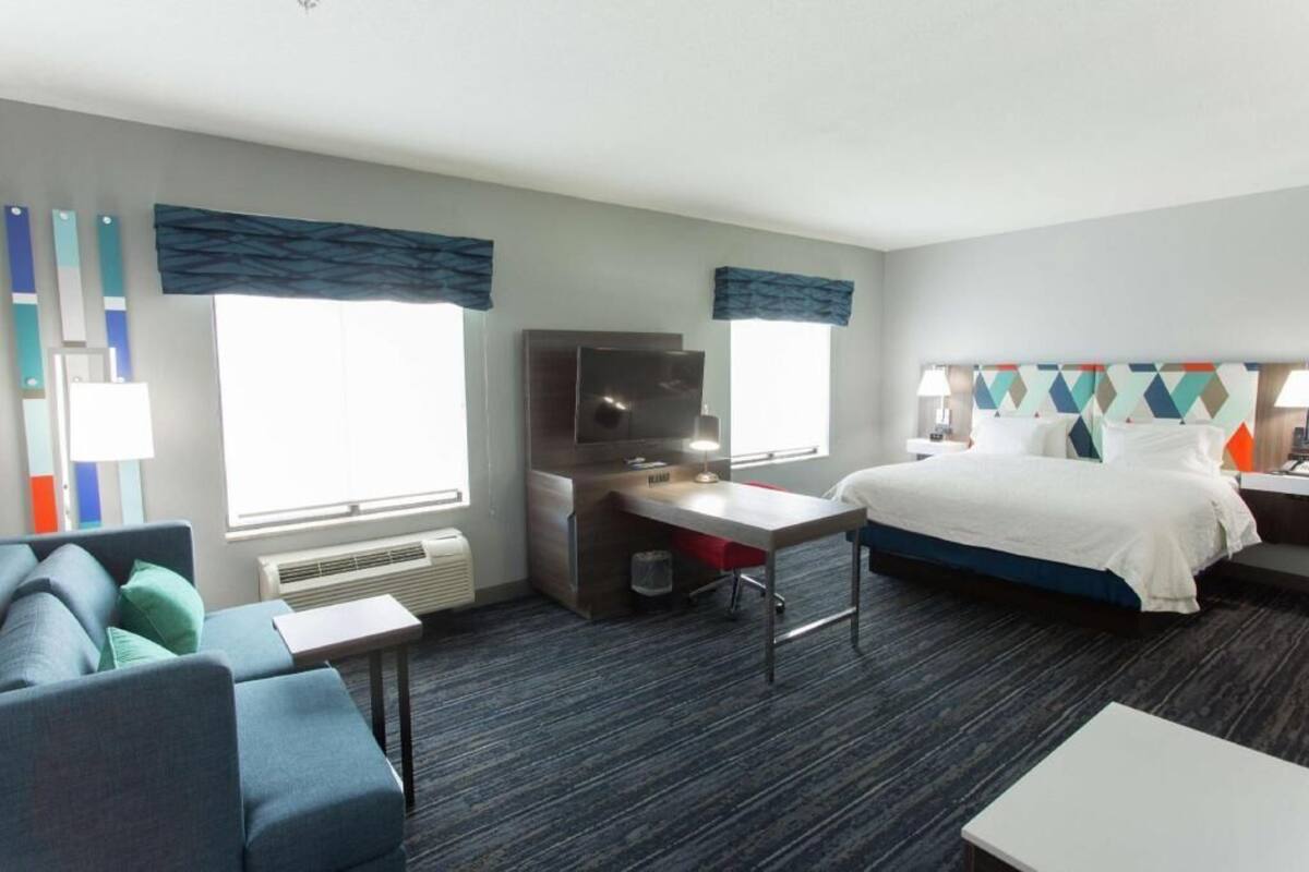A hotel room with a bed, a desk, a chair, a TV, and a window with curtains.
