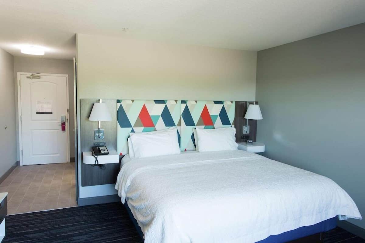 A hotel room with a bed, bedside lamps, a phone, and a wall-mounted headboard with a geometric pattern.
