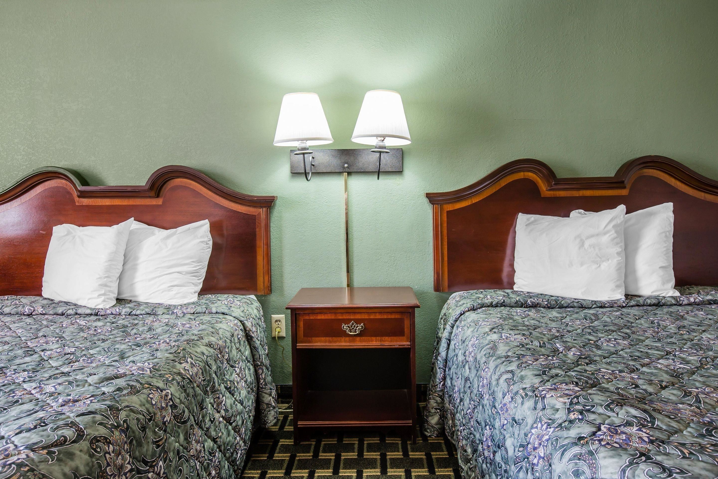 Une chambre d’hôtel avec deux lits, chacun doté d’une tête de lit en bois et d’oreillers assortis. Une table de chevet avec une lampe se trouve entre les deux lits.
