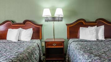 Une chambre d’hôtel avec deux lits, chacun doté d’une tête de lit en bois et d’oreillers assortis. Une table de chevet avec une lampe se trouve entre les deux lits.