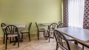 A dining area with a long table and several chairs, a tiled floor, and a window with patterned curtains.