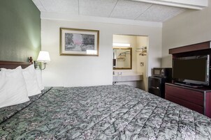 Quarto de hotel com uma cama grande, penteadeira, televisão, espelho e um quadro na parede.