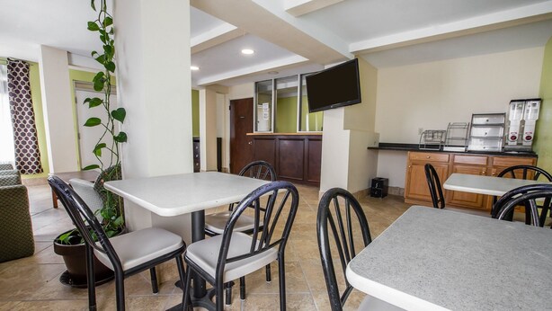 A dining area with tables and chairs, a television mounted on the wall, and a kitchen area with appliances. - Rodeway Inn Laurens (Laurens)